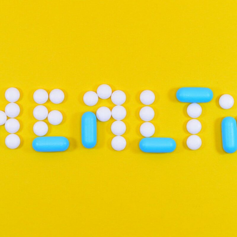 White and Blue Health Pill and Tablet Letter Cutout on Yellow Surface